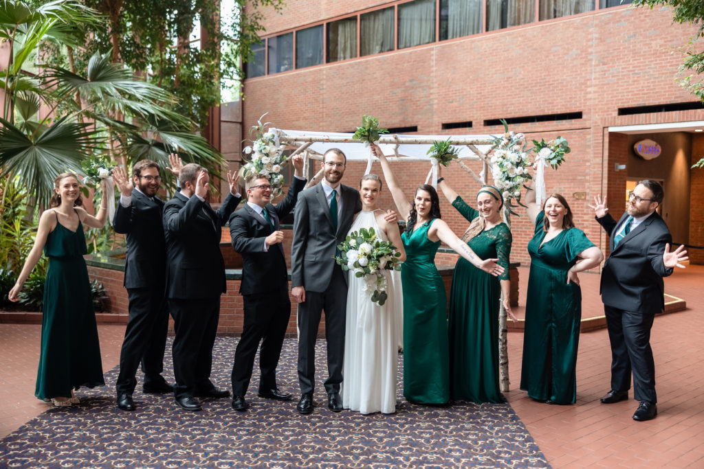 The wedding party gets excited for a portrait as they stand in front of the chuppah immediately following the atrium wedding ceremony.