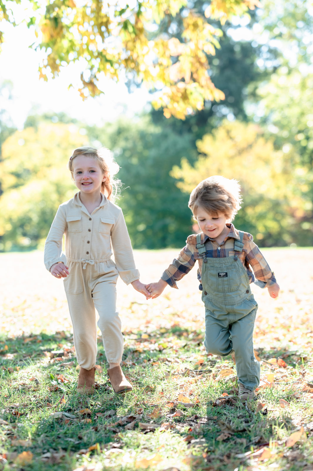 Brother and sister run towards the camera, smiling and holding hands during annual family portrait session.