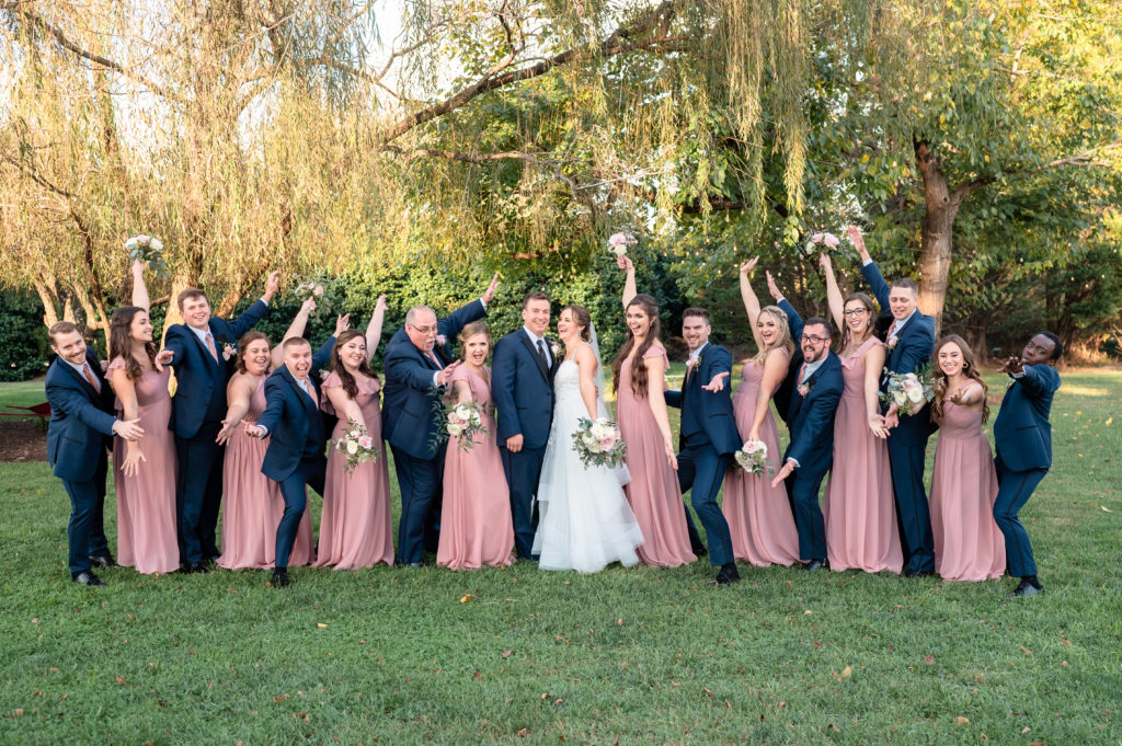 A group photo of the bridal party, with the bridesmaids in flowy, light pink dresses and the groomsmen in navy suits.
