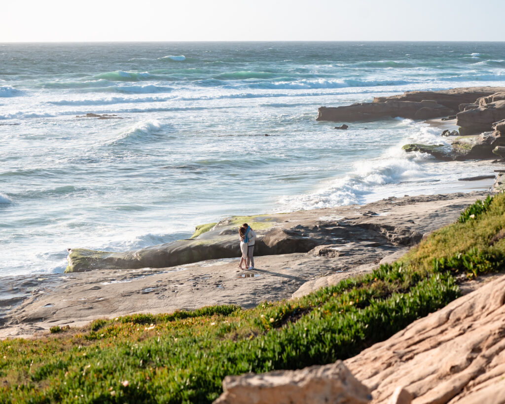 Jill and Reece embracing after the proposal with La Jolla's stunning coastline in the background