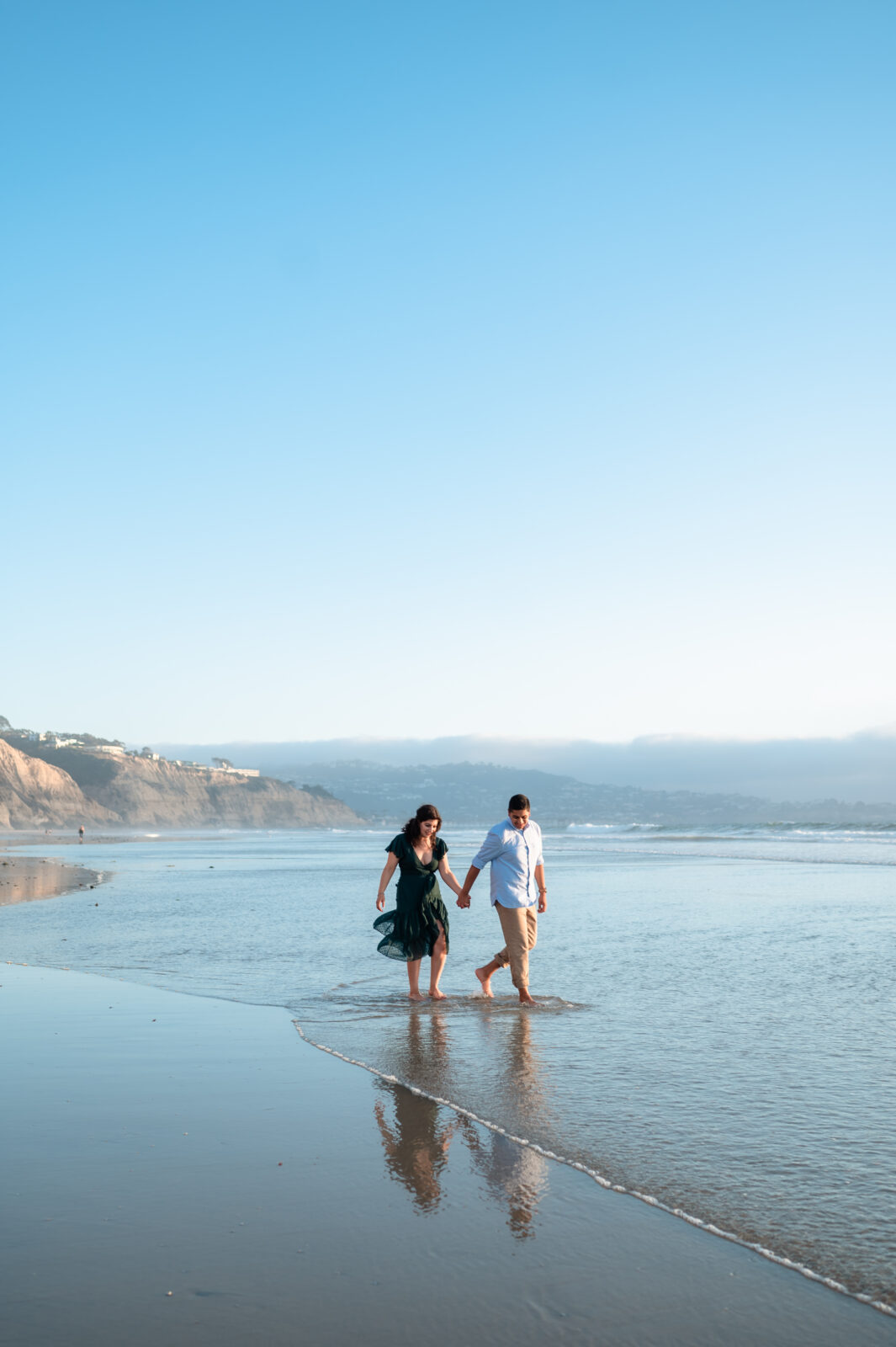 Couple walking arm-in-arm in a picturesque beach in one of our popular engagement photoshoot poses