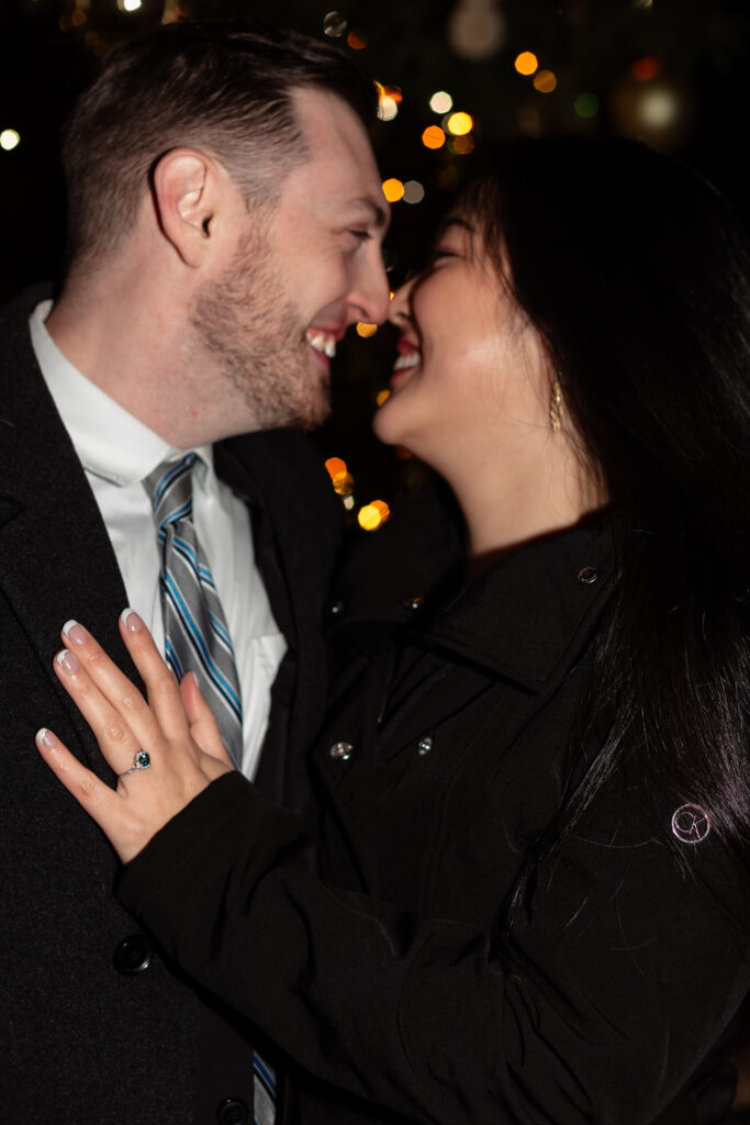 Close-up of Terri’s engagement ring with the holiday lights of Lewis Ginter GardenFest as a sparkling backdrop, photographed by EmmiClaire Photography.