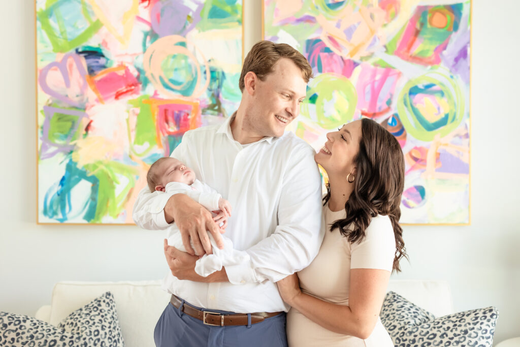 Mom and dad smiling at each other while holding newborn Baby Palmer during in-home lifestyle session in Richmond, Virginia