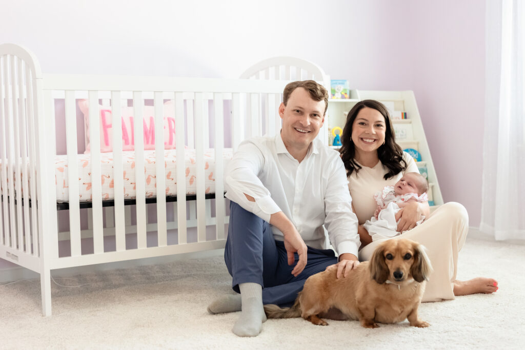 Parents sitting on nursery floor with newborn baby Palmer and their dachshund in Richmond, VA home