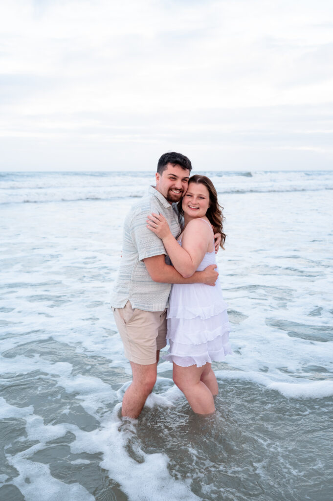 Waves crashing gently behind the couple during their beach engagement session