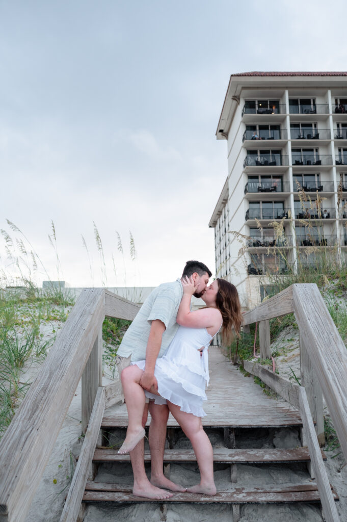 Romantic post-proposal moment of Jack and Emily on the boardwalk with One Ocean Resort in the background