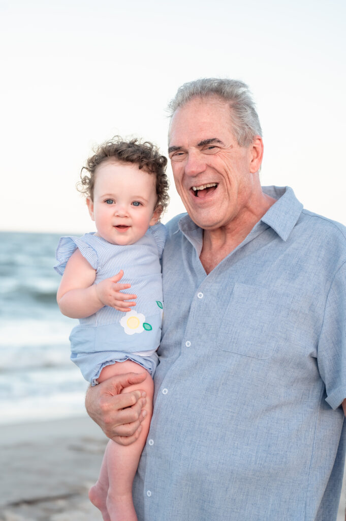 Grandfather and granddaughter smiling together in a portrait shot in front of the ocean during blue hour.