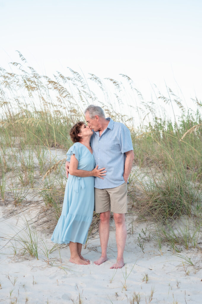 Grandparents sitting in the sand with their grandchildren gathered around them for a joyful portrait.