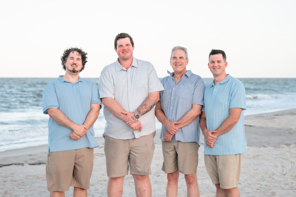 A father posing with his sons in front of the blue ocean and golden evening light in the background.