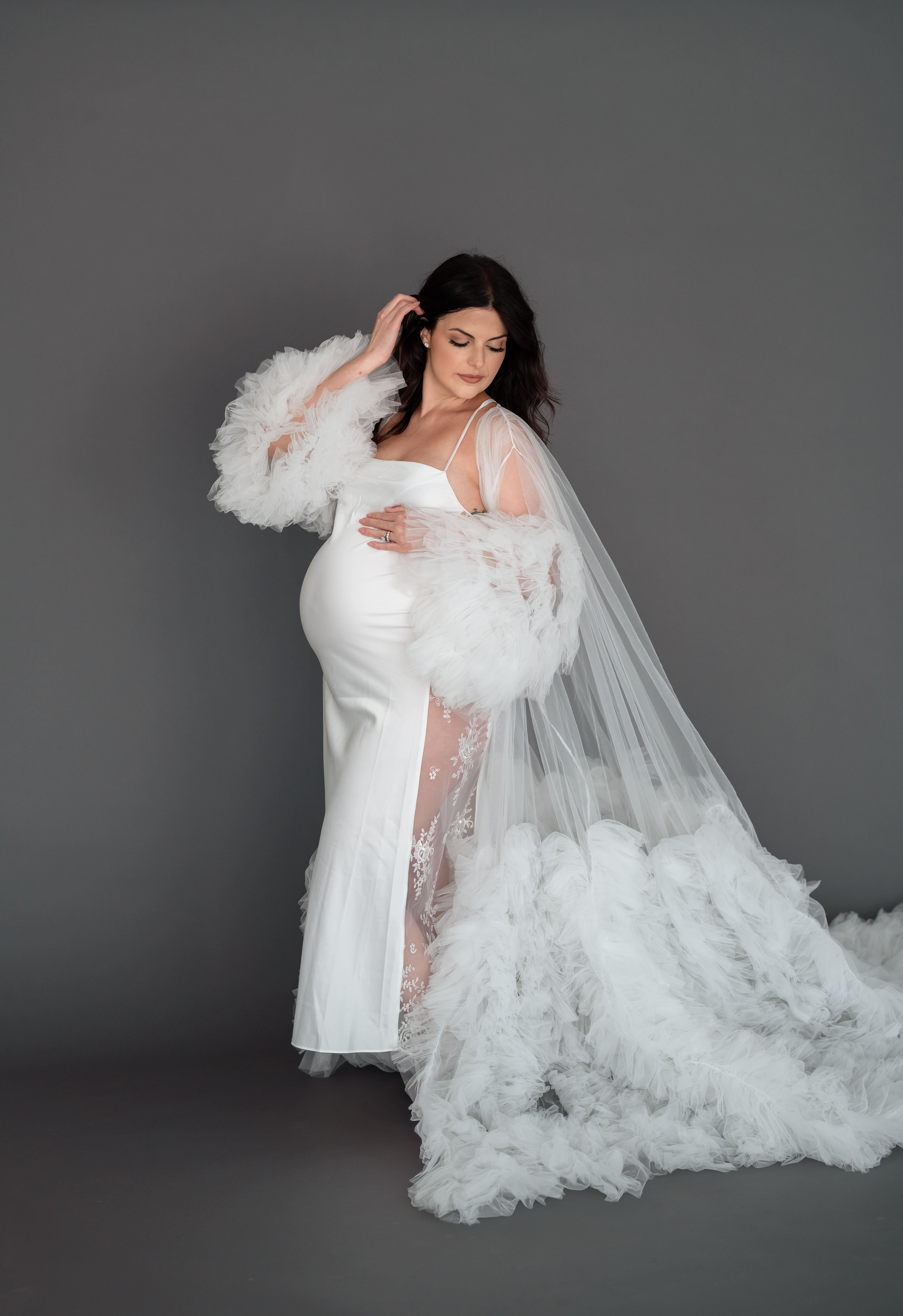 Mom holding belly against curtain backdrop at studio maternity session.
