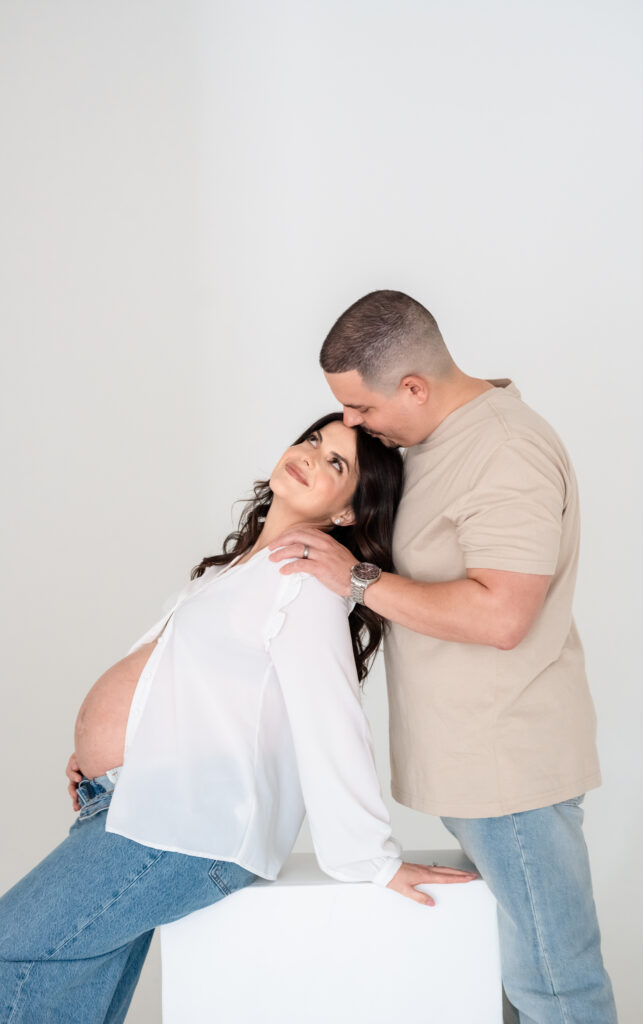 Couple embracing and smiling during studio maternity session.