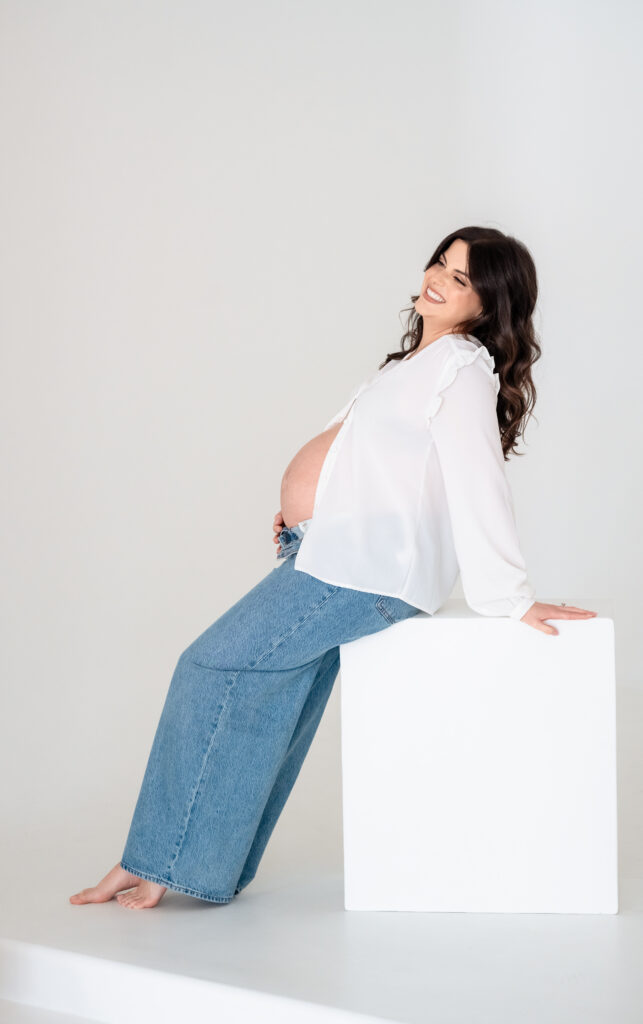 Mom leaning on wall in natural light during studio maternity session