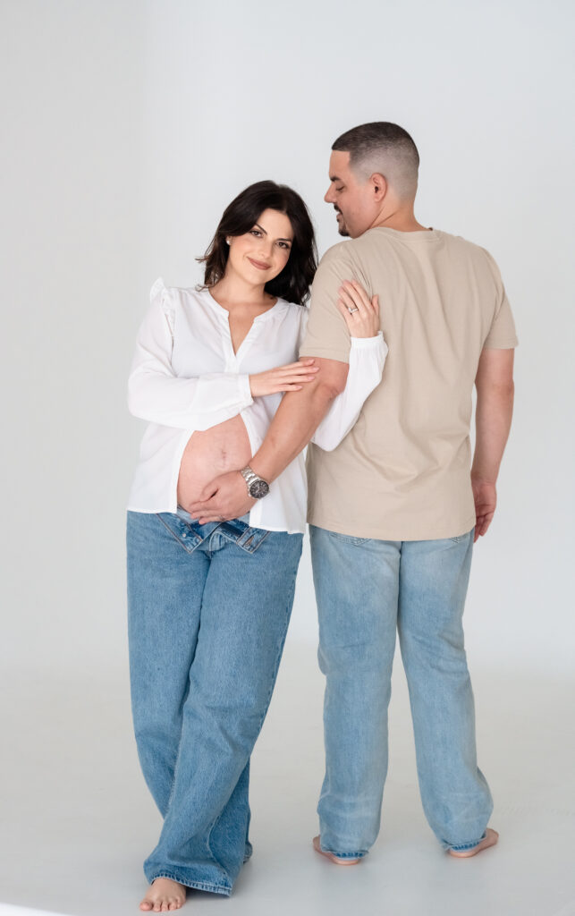 Couple smiling together in gray backdrop studio maternity session.