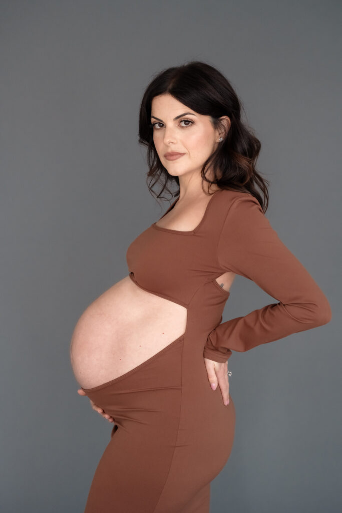 Side profile of baby bump in brown dress at studio maternity session.