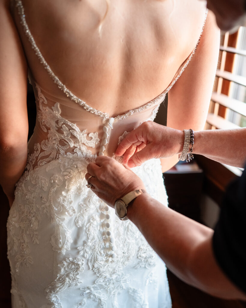 Bride getting zipped into her wedding dress with a sweet candid moment