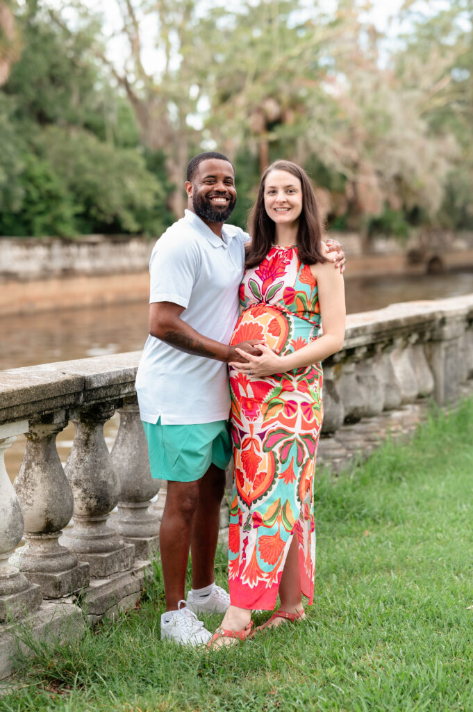 Maternity photos at Yacht Basin Park Jacksonville with couple standing by the waterfront stone railing