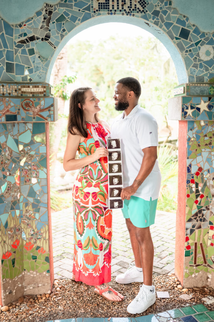 Pregnancy announcement at Yacht Basin Park gazebo with couple holding ultrasound beneath mosaic arch