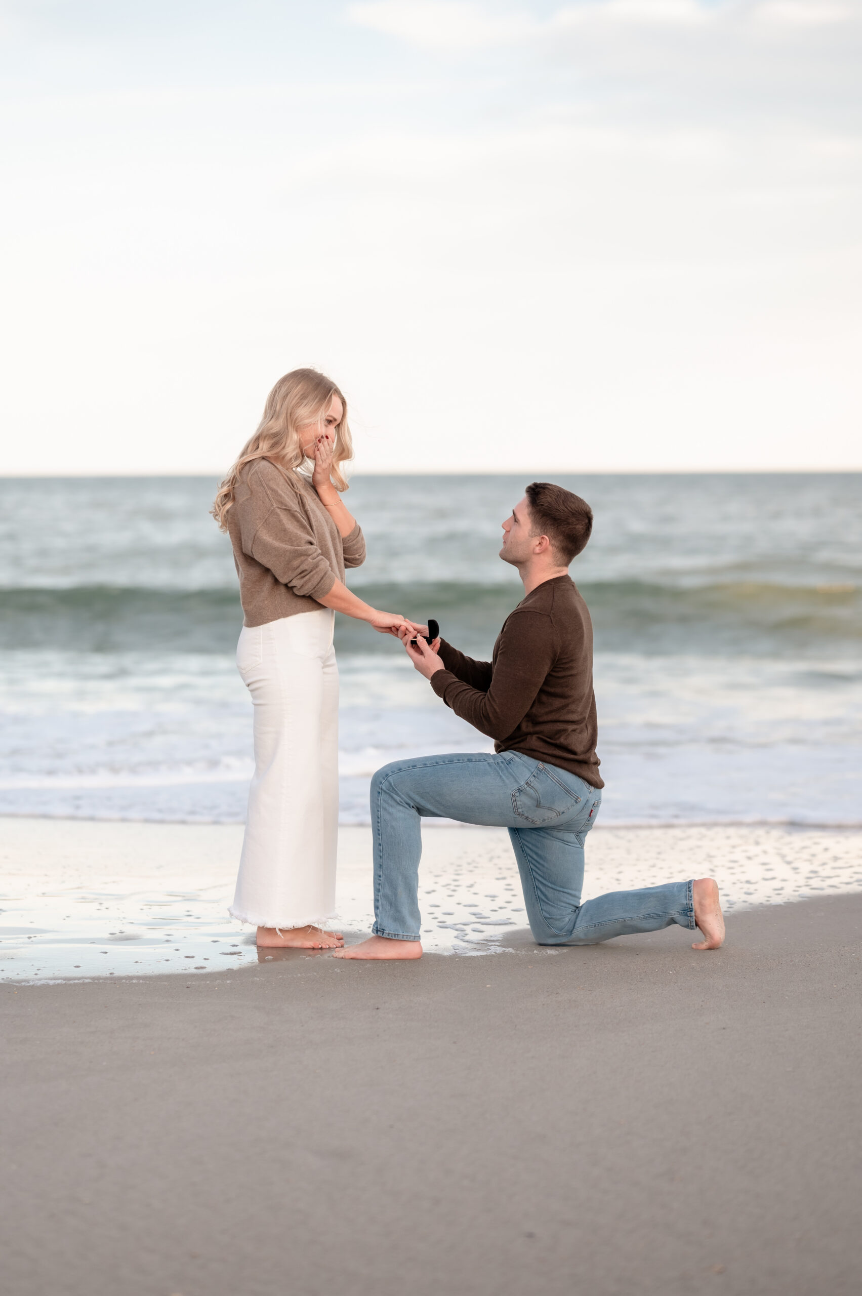 Chase proposing to Rachel on the sand during a sunset surprise proposal at Jacksonville Beach.
