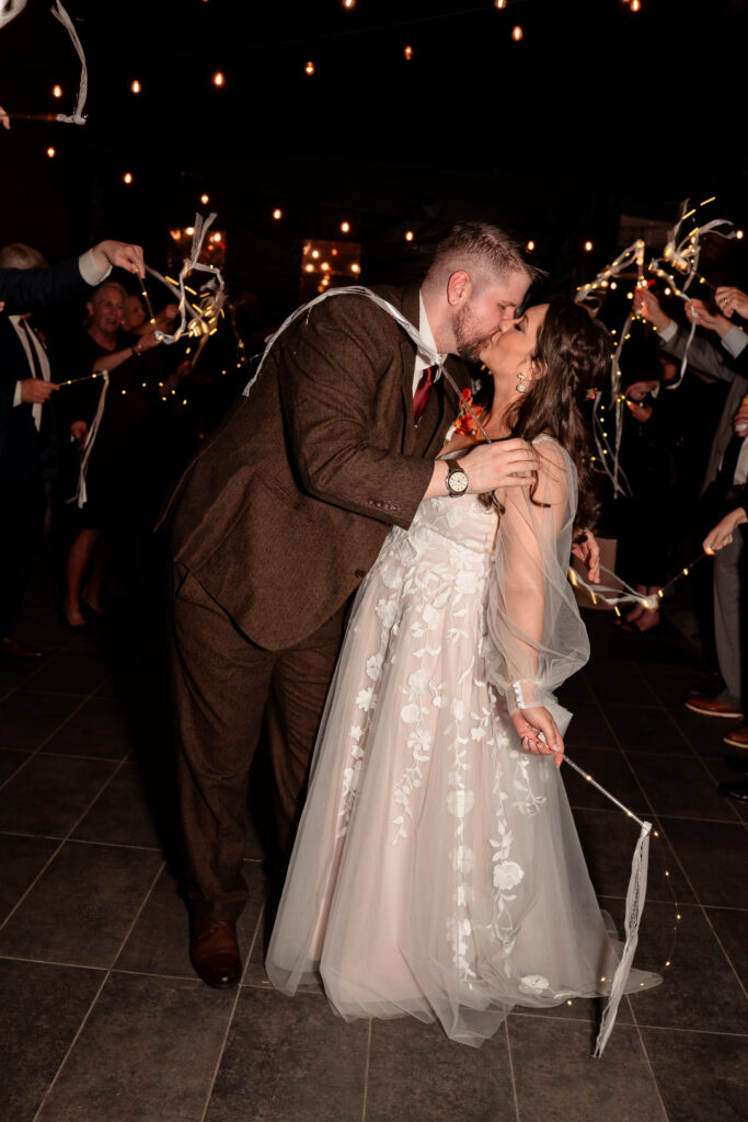 Bride and groom exiting their wedding celebration through a ribbon send off surrounded by guests.