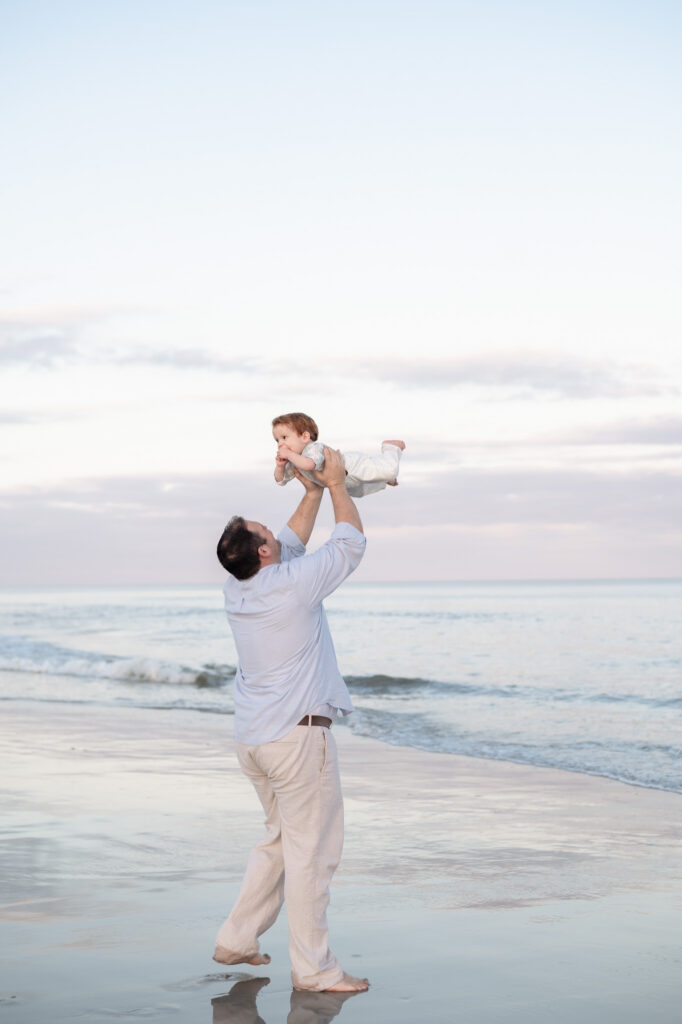dad lifting baby in air ocean background